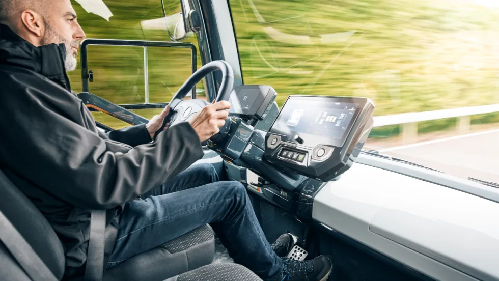 Man inside the cab of a futuristic looking truck driving.