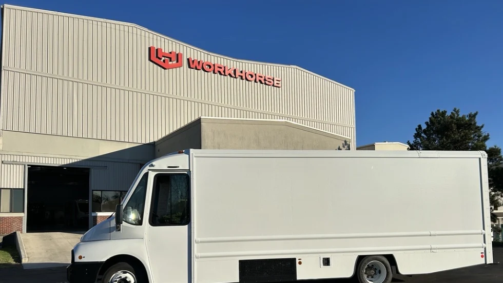 Side view of an electric step van parked in front of a building with a Workhorse sign.