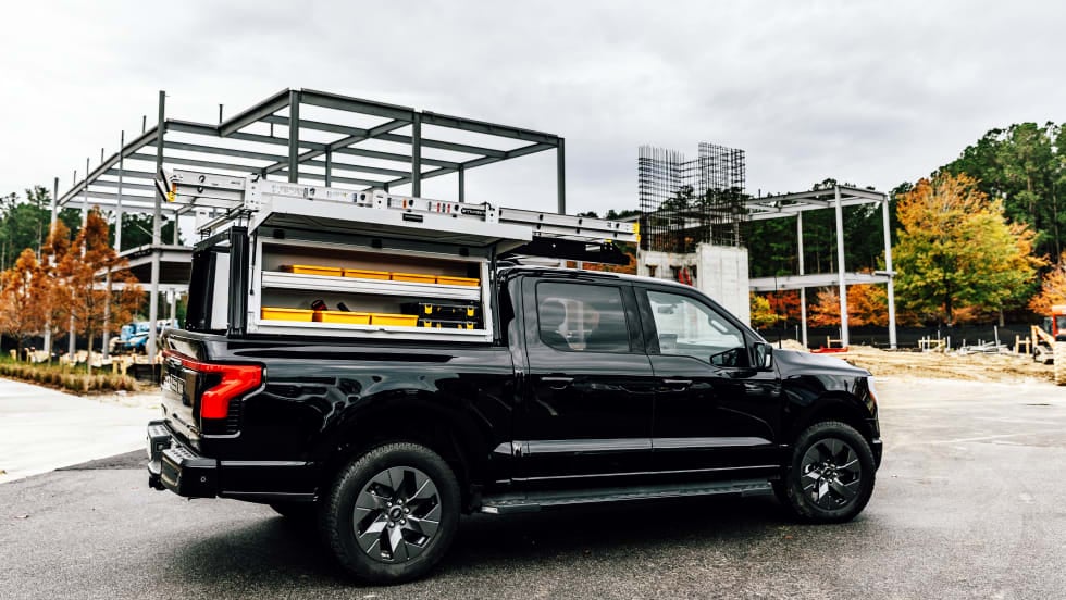 Side view of a black pickup truck with a work truck cap over bed and shelving shown in the sides.