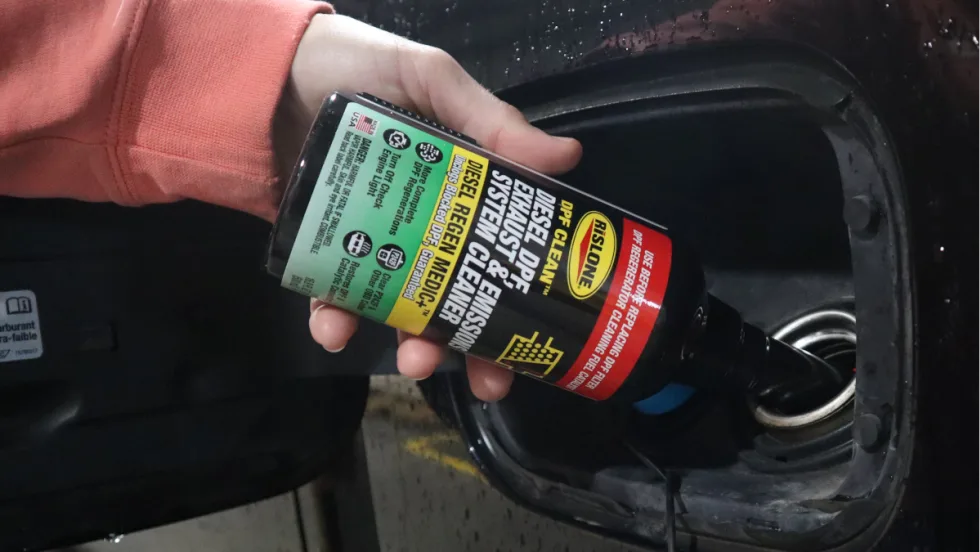 Closeup of hand touring bottle of DPF cleaner into a fuel tank.