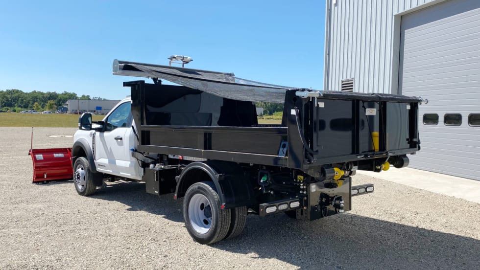Rear quarter view of a dump body pickup with a tarping system covering the dump.