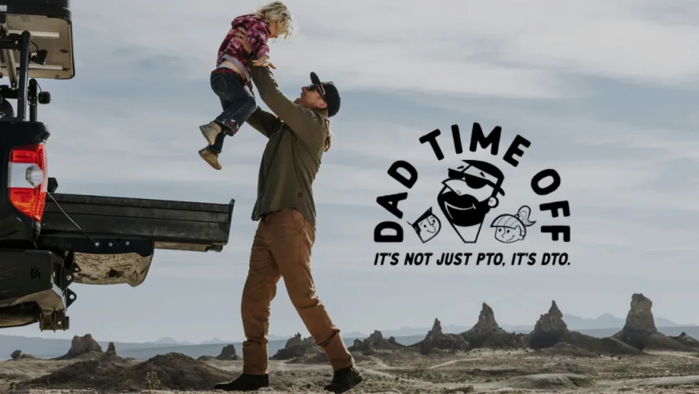 A dad lifts his child near a truck bed in a desert setting with the DECKED Dad Time Off logo and slogan: “It’s not just PTO, it’s DTO.”