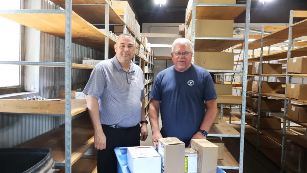 Two men standing in a parts warehouse with shelving and boxes.