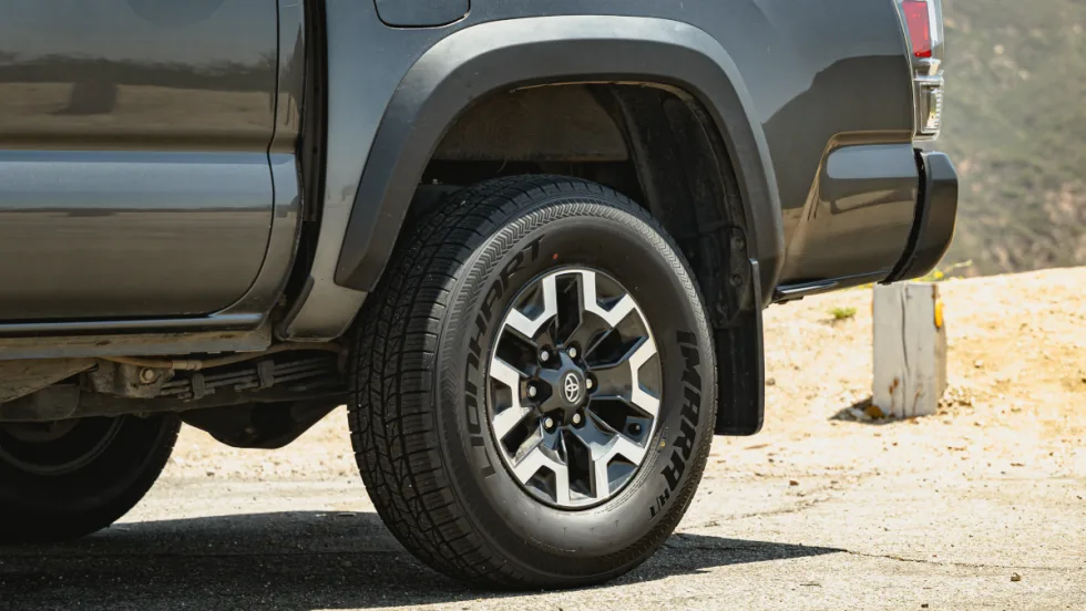 Closeup photo of the rear left tire of a pickup truck parked in a dirt area.