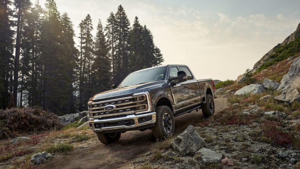A 2026 Ford Super Duty pickup truck driving on a rocky trail in a mountainous forest setting.