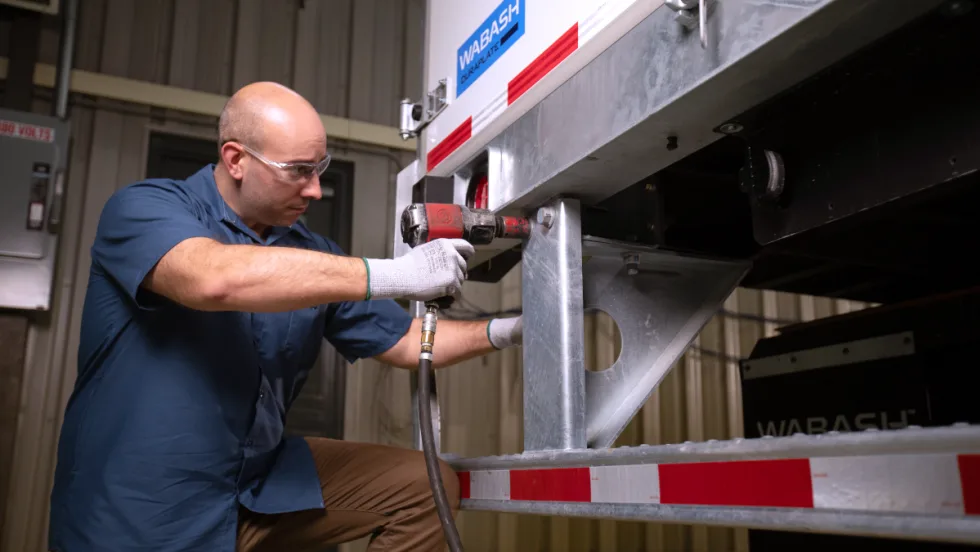 Maintenance technician working on a Wabash trailer, at the rear.