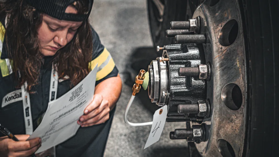 Technician reviewing paperwork while inspecting a truck wheel hub during Top Tech contest.