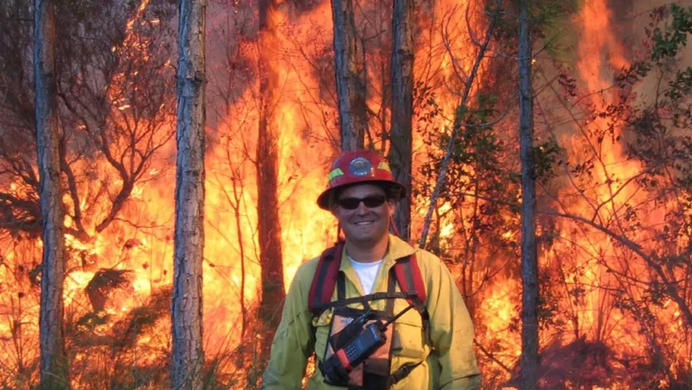 David Ronsen in firefighter gear standing in front of a raging wildfire during his early firefighting career.