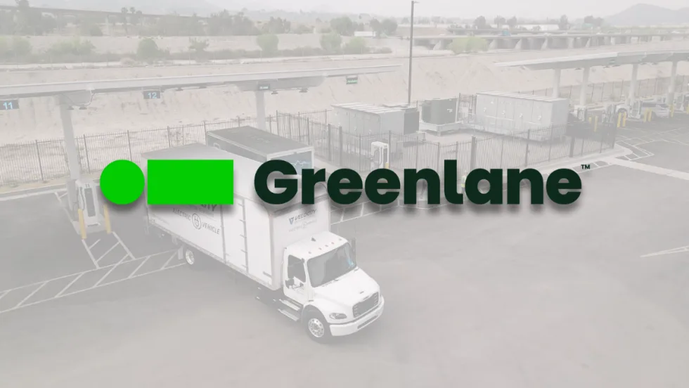 Greenlane logo overlaid on a picture of a Velocity electric truck parked at Greenlane’s Colton, California charging site with multiple charging stations visible.