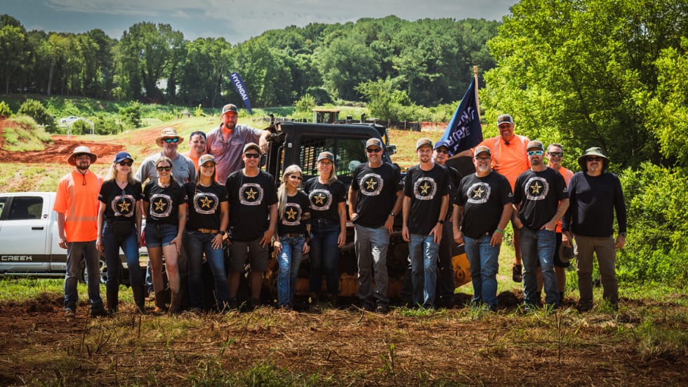 Group of National Equipment League operators and staff standing outdoors in front of equipment and trucks.