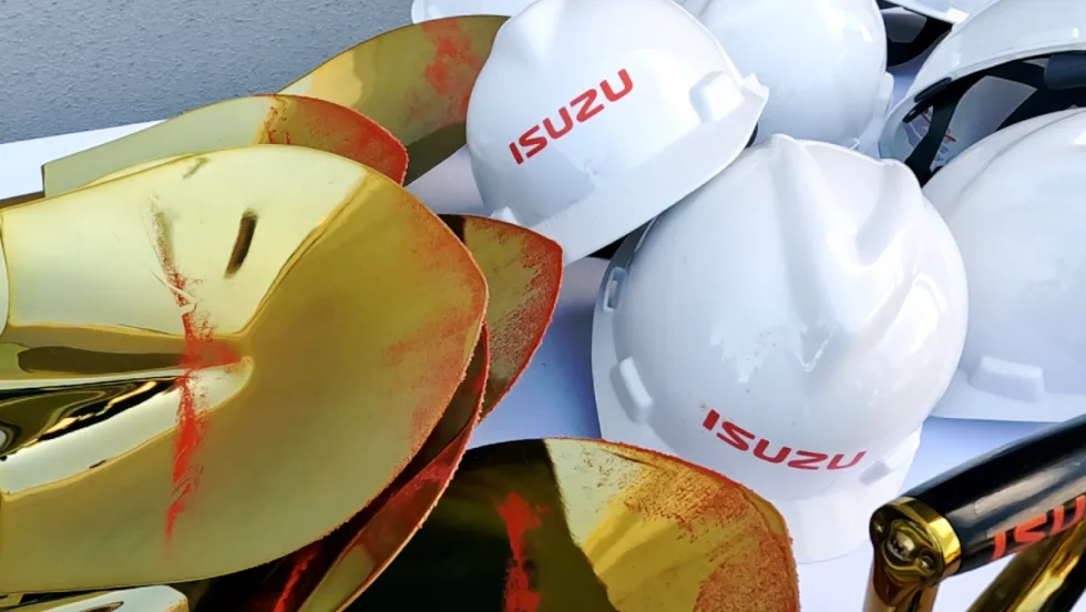 A collection of Isuzu hardhats and shovels, which have a dusting of red dirt.