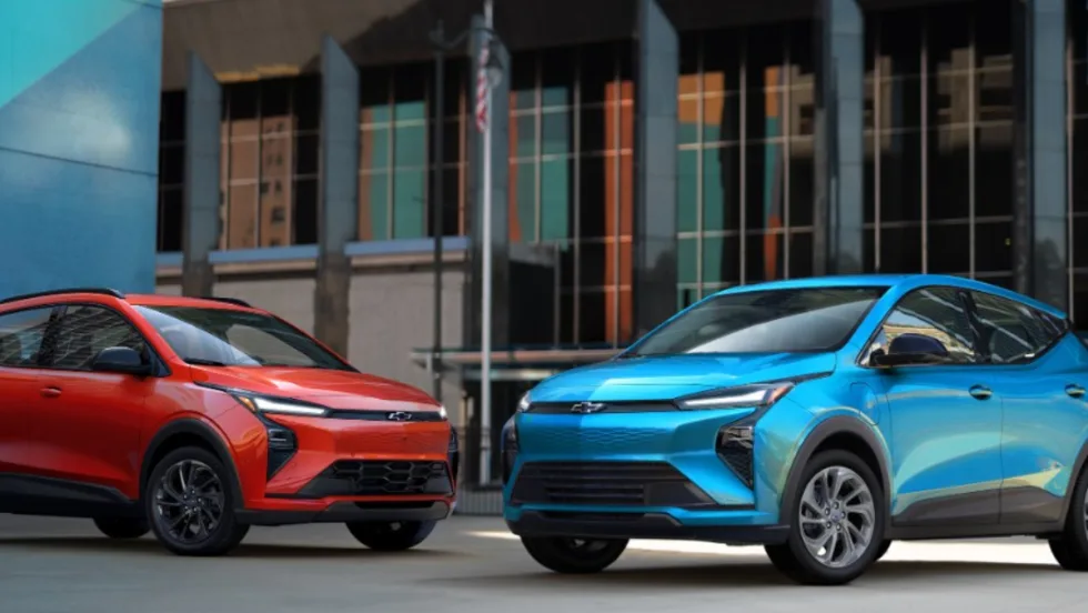 Blue and red 2027 Chevrolet Bolt EVs parked side by side in an urban setting.