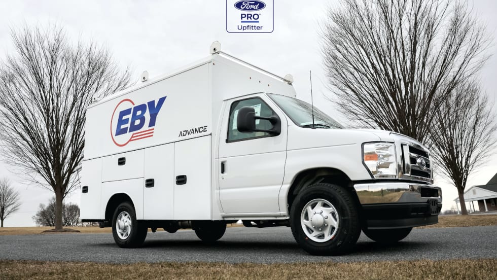 A white service van with a white box body and logo for Eby on the side, with Ford Pro logo against the sky.