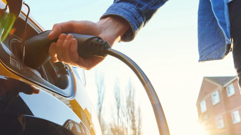 Person plugging an electric vehicle charger into a car outdoors in daylight, representing versatile charging options for different connector types.