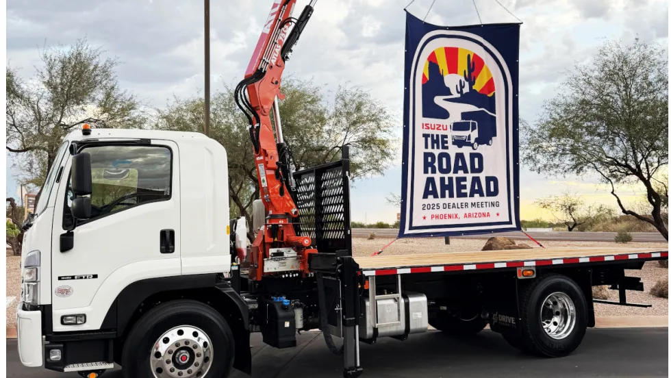 Flatbed Isuzu truck with a sign on back promoting The Road Ahead, the company's annual dealer meeting.