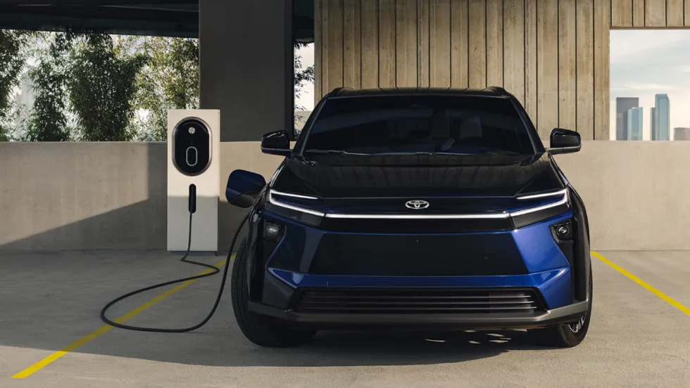 Front view of a Toyota bZ electric vehicle parked at a public charging station in an urban setting.