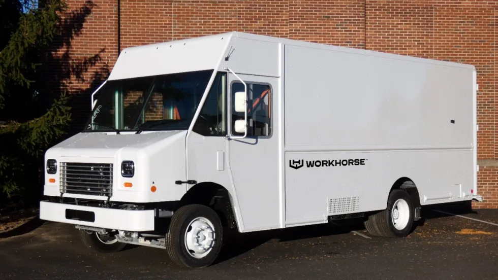 Front quarter view of a white step van parked next to the brick wall of a building.