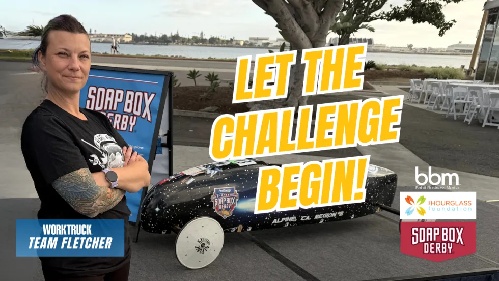 Lauren Fletcher stands with arms crossed beside a black soap box derby car at a waterfront venue. Text on image reads “Let the Challenge Begin” Work Truck, Hourglass Foundation, and Soap Box Derby