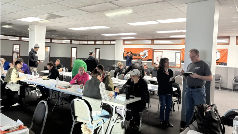 Group[ of people working and talking in a classroom setting.