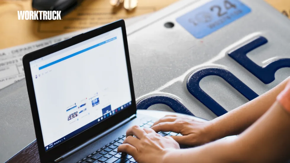 Person using a laptop beside a vehicle license plate, representing how fleets use technology to manage registrations, track renewals, and stay compliant across multiple jurisdictions.