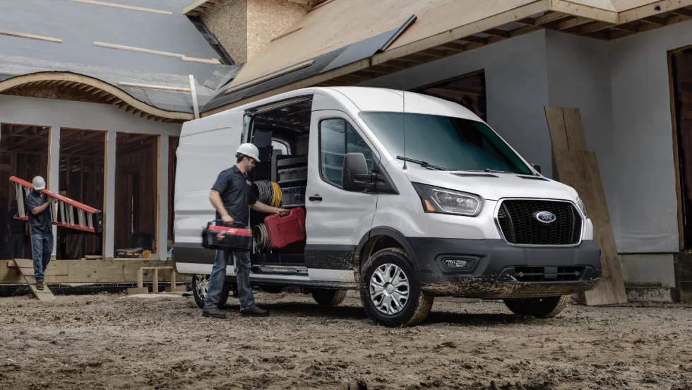 2026 Ford Transit Cargo Van parked at a construction site with a worker loading tools. Photo highlights real world fleet use and new tech updates designed to support daily commercial operations.