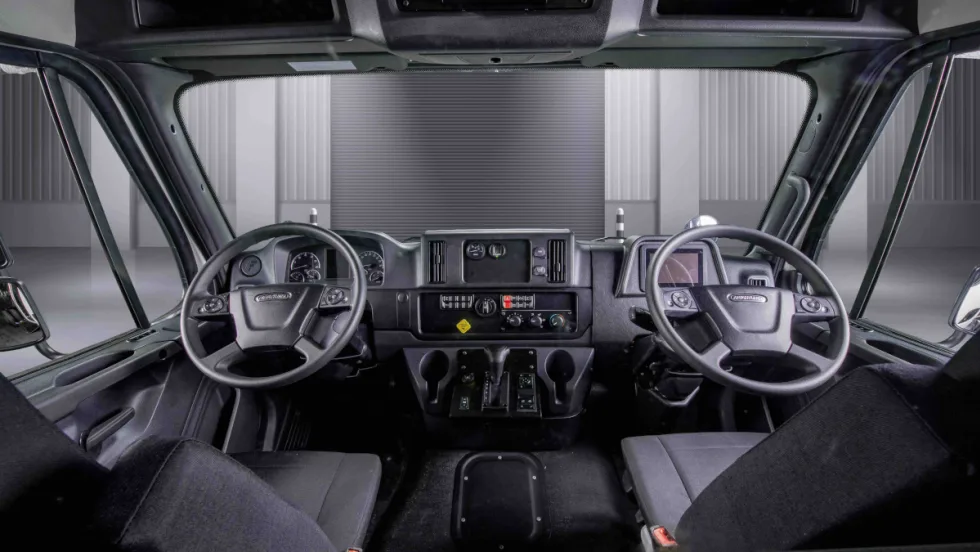 Interior view of a truck cab looking forward toward two steering wheels, one left and one right.