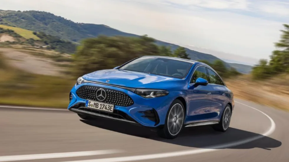 Blue Mercedes-Benz sedan driving on a curving road with blurred hills in the background.