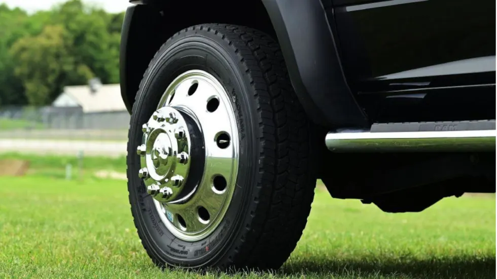 Closeup photo of a front left truck tire on a black truck parked on grass.