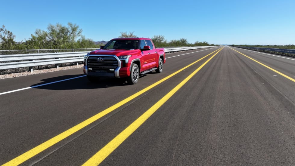 Red Toyota pickup truck driving down road with two spaced yellow lines and driving toward the camera.