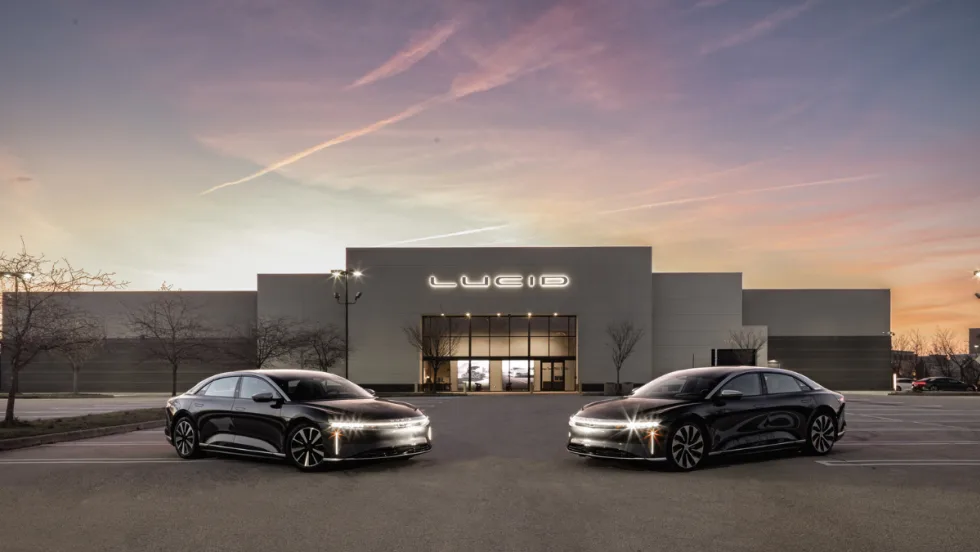 Two Lucid electric sedans parked in front of a Lucid facility at dusk, representing the automaker’s new certified pre-owned vehicle program.