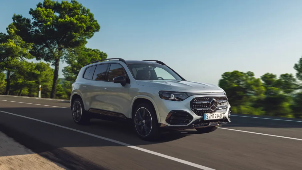 All-electric Mercedes-Benz GLB compact SUV driving on a paved road, shown in a front three-quarter view with updated exterior design and lighting.
