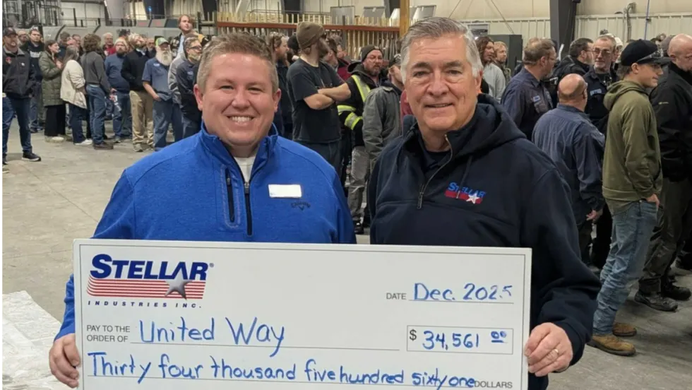 Photo or one man presenting a large check to another man with people in the background.