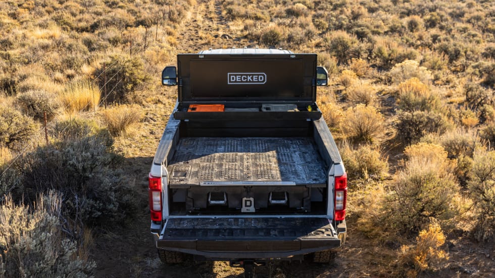 Rear view of a pickup with a DECKED tool box mounted at the front of the open bed in an outdoor setting.