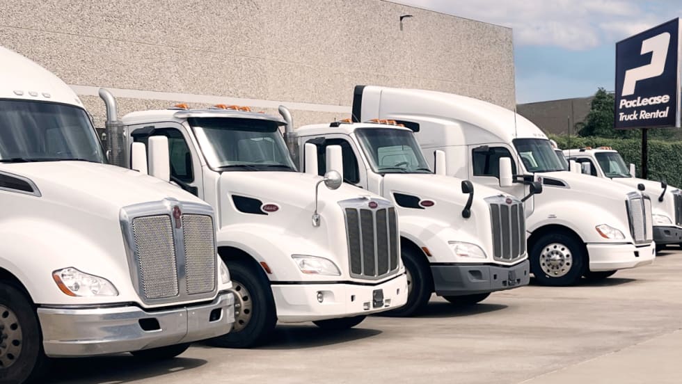 Row of five truck cabs parked outside a building with a PacLease sign in the background.