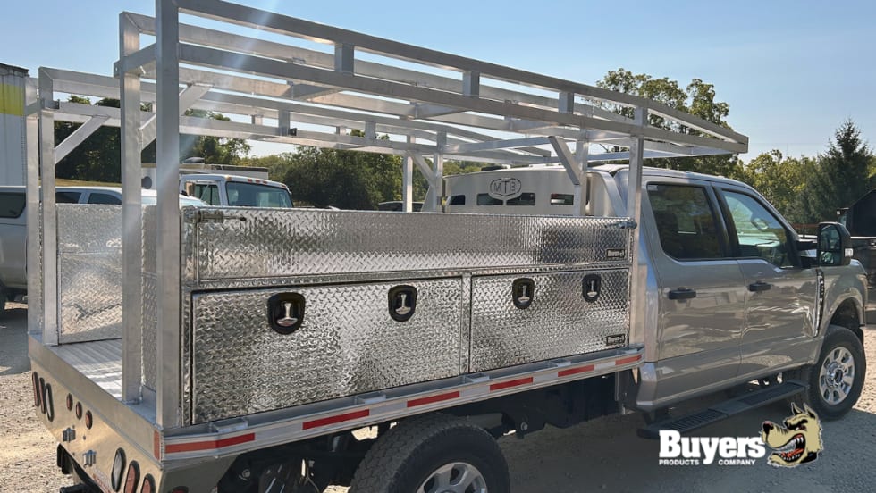 Side view of a work truck with multiple tool boxes and storage bins and a ladder rack on top.