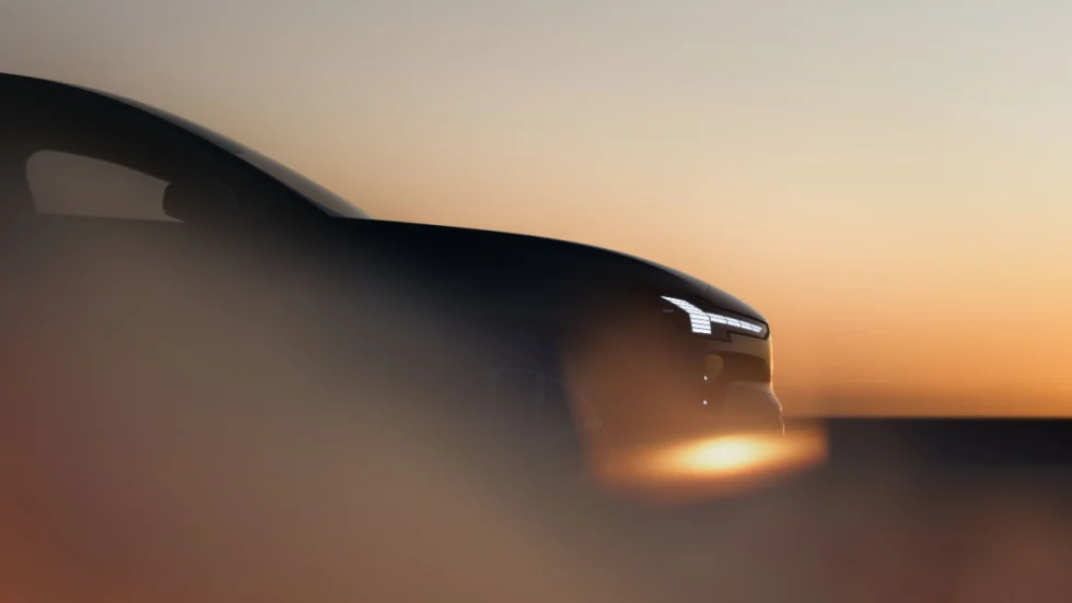 A dark, stylized side view of a vehicle at sunset, with headlights visible.