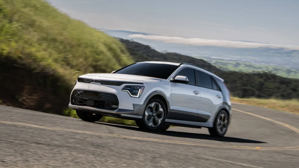 2026 Kia Niro EV driving on a winding road through a hilly landscape.