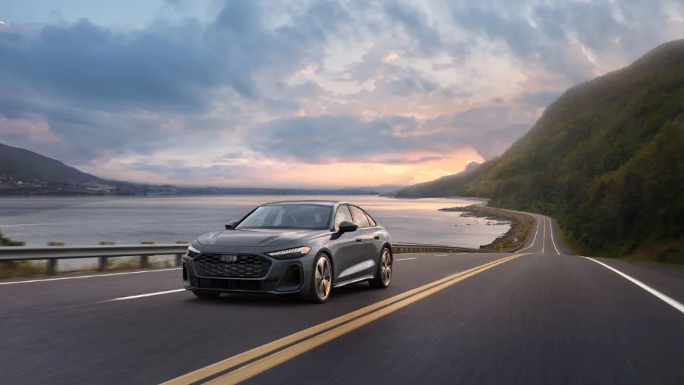 A 2026 Audi A5 driving on a highway near water and hills.