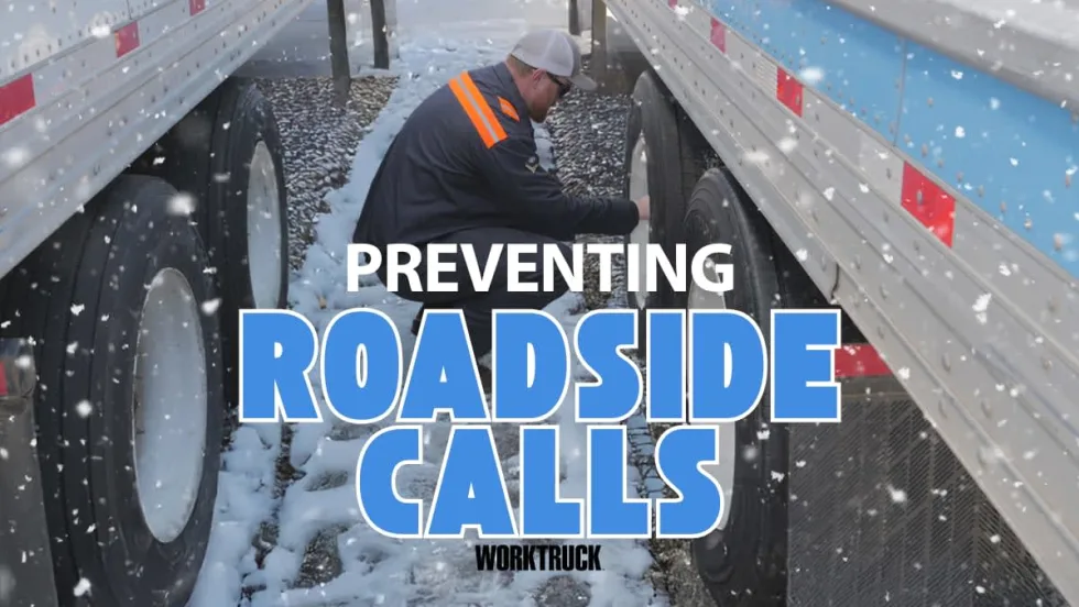 Technician checks semi-truck tire pressure in snowy yard between trailers to help prevent winter breakdowns and roadside calls.