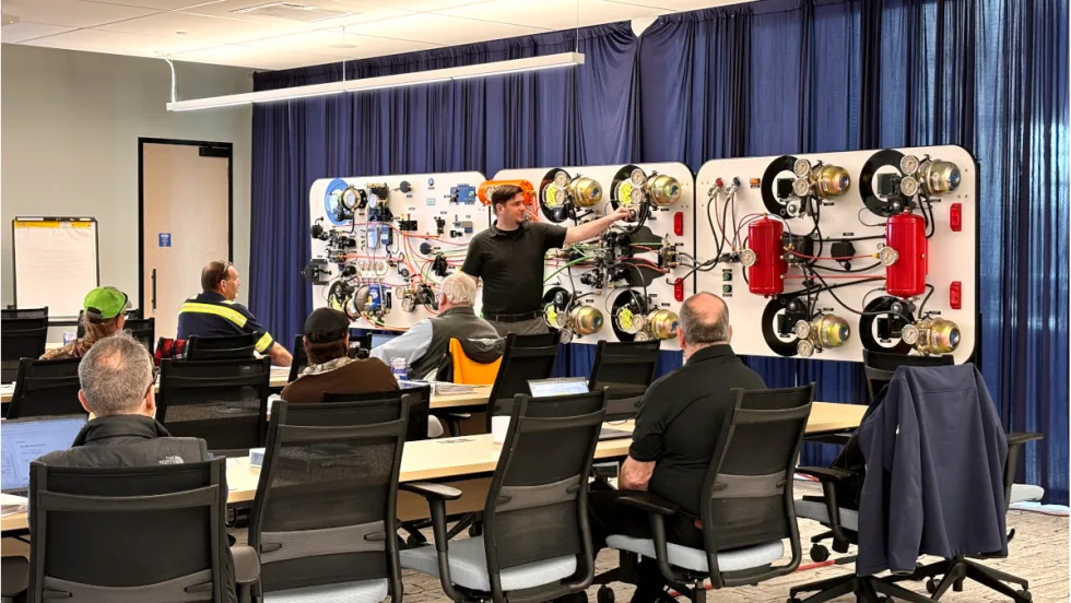 Group in classroom listens as an instructor in front of room demonstrates an air brake system and its components.
