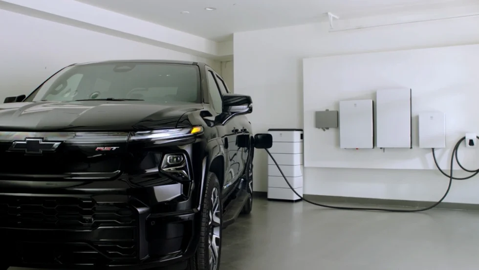 Chevrolet Silverado EV plugged into a home energy system with wall-mounted battery and power management units in a residential garage.