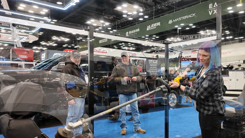 Demonstration at a trade show showing a person using a weed whacker against a protected truck seat to test Tiger Tough durability.