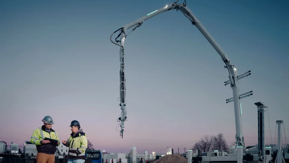 Dark blue sky at dusk, two construction workers, a crane-type structure in the background.