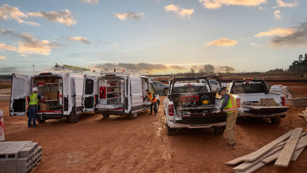 Fleet of work trucks and vans with open doors showing organized storage systems at a jobsite.