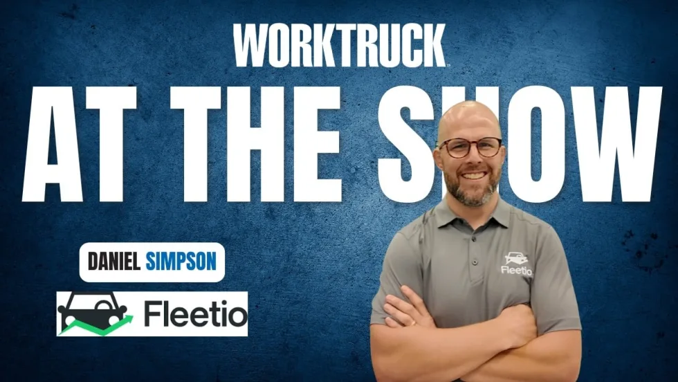 Man standing with arms crossed in front of blue background with Work Truck logo and At The Show in large white letters, plus a Fleetio logo.