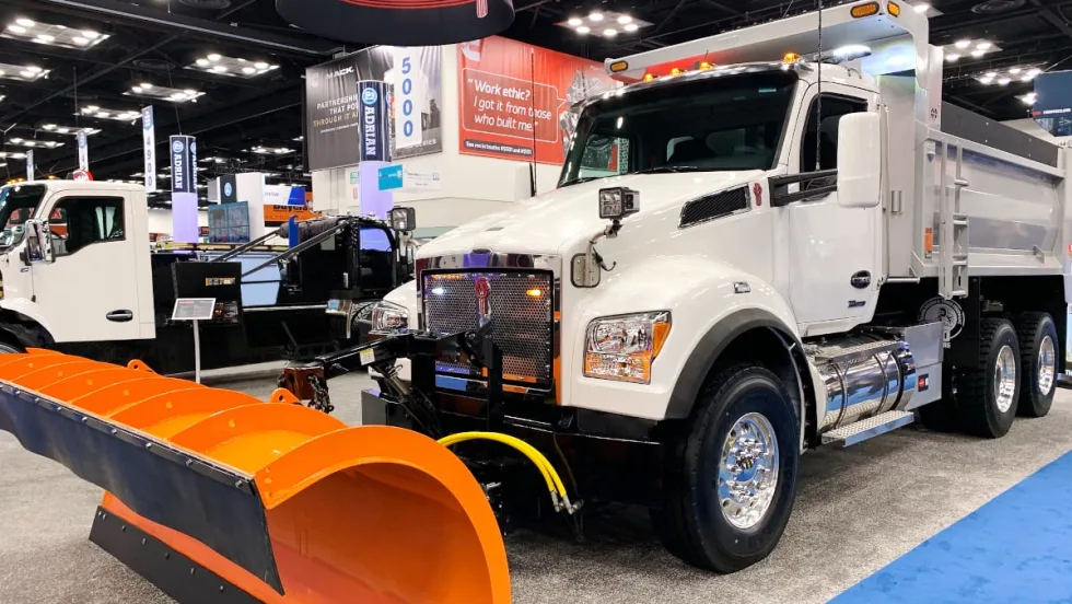 Front angled photo of a white dump truck with an orange snow plow on the front.