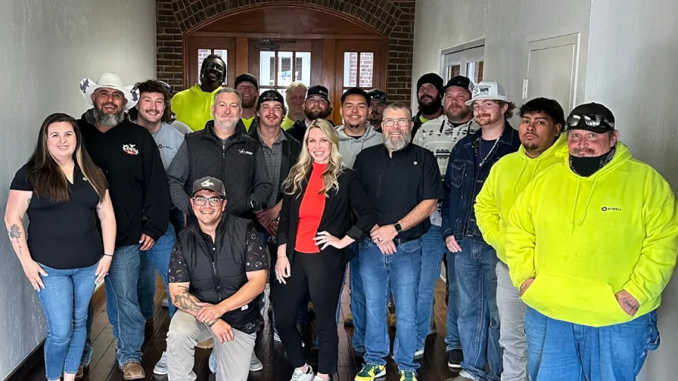 A group of Atwell employees gather indoors for a team photo, standing together