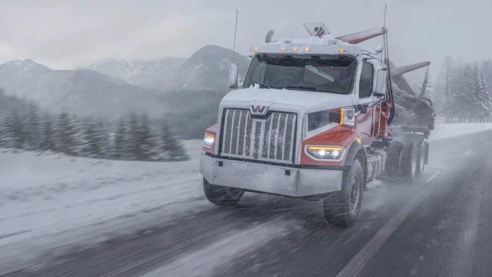 Western Star truck hauling logs through a snowy mountain road during a winter storm, highlighting extreme cold durability and performance testing.