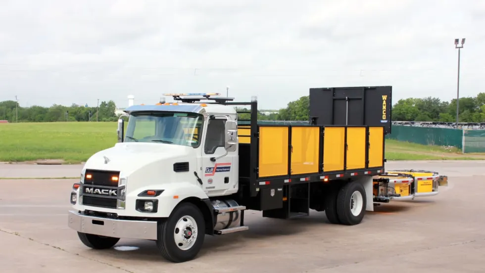 White work truck with yellow bed and yellow rear-mounted crash protection device parked in a parking lot.