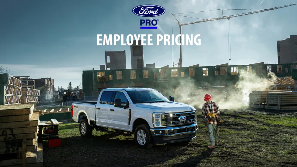 White Ford Super Duty pickup truck parked at a construction site beneath a Ford Pro Employee Pricing banner.
